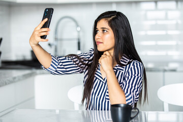 Attractive young indian woman making selfie in the kitchen.