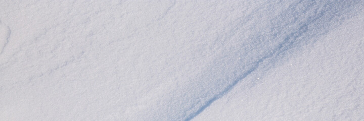 Fototapeta na wymiar Beautiful winter background with snowy ground. Natural snow texture. Wind sculpted patterns on snow surface. Wide panoramic texture for background and design. Closeup top view with copy space.