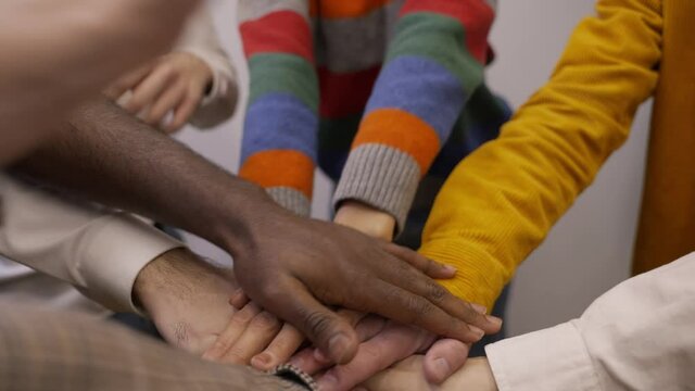 Stack of joined hands with different skin tone, happy multiethnic colleagues rejoicing at successful and profitable teamwork. Cheerful diverse team joining hands and raising arms up expressing delight