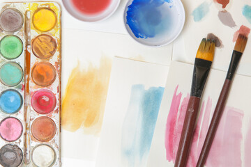 Watercolor paints palette, brushes and papers on table. Creative hobby or art therapy concept.