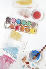 Watercolor paints palette, brushes and papers on table. Creative hobby or art therapy concept.