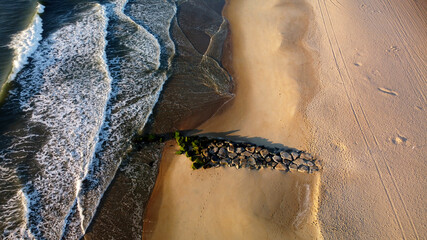 Aerial view of a rock jetty and waves on the beach