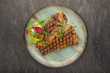 Grilled beef steak with rosemary, salt and pepper on black stone plate. Grilled striploin sliced steak. Juicy thick grilled beef steak seasoned with rosemary fresh of the summer BBQ.