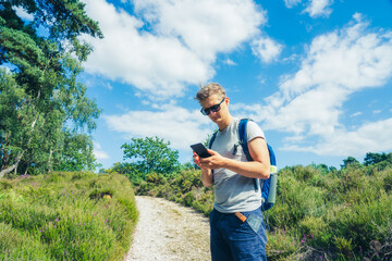 Young Male tourist with backpack using smartphone navigation app during hiking walk in the summer...