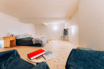 Simple bedroom in loft apartment in wooden style with double bed, bedside tables and two glasses of wine with bottle on tray.  Bedroom is lit by tow bright lights mounted on wall.