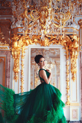 Portrait of a beautiful young girl in a haute couture green dress standing in a luxurious gold interior.