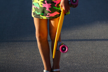 Defocus girl holding yellow penny board. Front view. Youth hipster culture. Child hands holding...