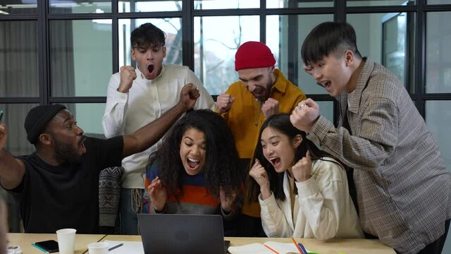 Team of multiracial co-workers with bated breath watching quotations on stock exchange at laptop and enthusiastically reacting to soaring of company's shares. Cheerful colleagues during stormy joy