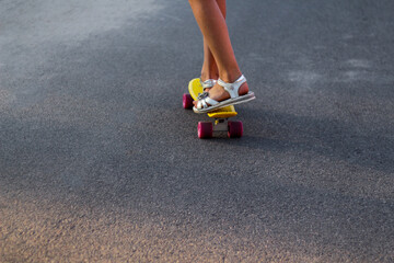 Defocus skater moving along asphalt road on a yellow skateboard wearing white sandals. Some of the legs are on a skateboard close up. Young sport activity. Leisure activity. Penny board. Out of focus