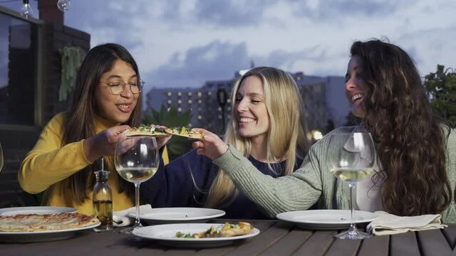Multiracial people eating dinner and drinking wine together outdoor at bar restaurant - Friends celebrating with pizza