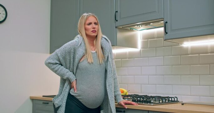 A pregnant woman begins to experience labor contractions while standing in the kitchen.