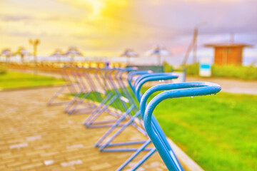 Bike Parking places on the ocean. Sea beach at sunset. Beach umbrellas and sun beds in the background. Green lawn and comfortable paths for cyclists. Weekend holidays, summer vacation.