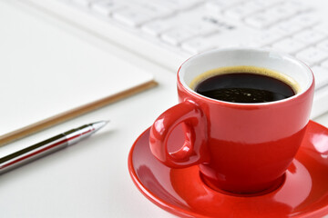 Close-up view, Black coffee in red cup on table desk with silver pen, book and keyboard is blurred background.