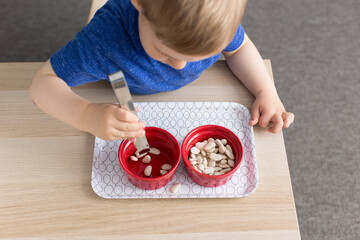 Little boy transferring  bean manipulatives into ceramic dishes, practicing practical living skills during his montessori education