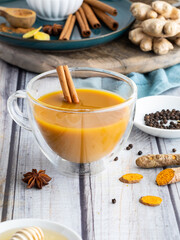 Golden turmeric milk in a tea cup with a cinnamon stick, surrounded by ingredients to make golden milk.