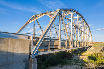 A Parker through truss bridge over a wash, dry river bed, foundations, shrub, blue sky along historic route 66, side view, Rio Puerco, New Mexico