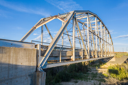 A Parker through truss bridge over a wash, dry river bed, foundations, shrub, blue sky along historic route 66, side view, Rio Puerco, New Mexico