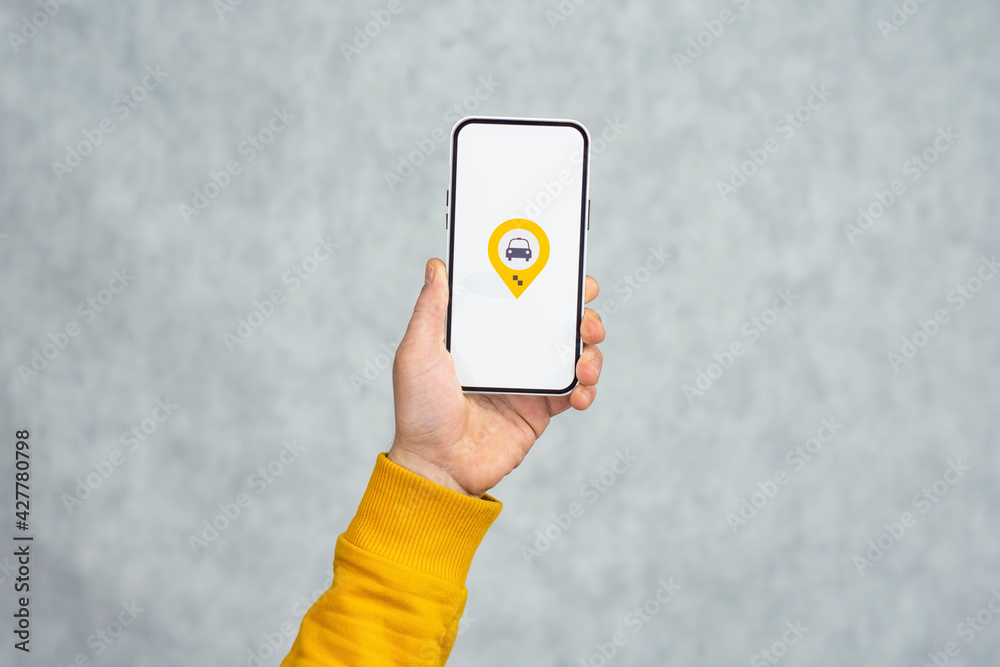 Wall mural phone display with taxi icon on light background. man holds a mockup smartphone in his hand close-up