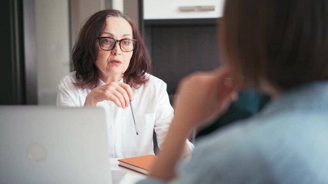 Middle-aged old businesswoman manager mentor speaking to a client offering insurance banking services deal teaching intern or convincing customer.