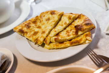 Freshly baked khachapuri bread with melted burnt cheese on a white plate in a restaurant