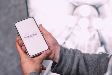 Phone display with a breaking news icon set against a backdrop of studio lighting. A man holds a mock-up of a smartphone in his hand close-up.