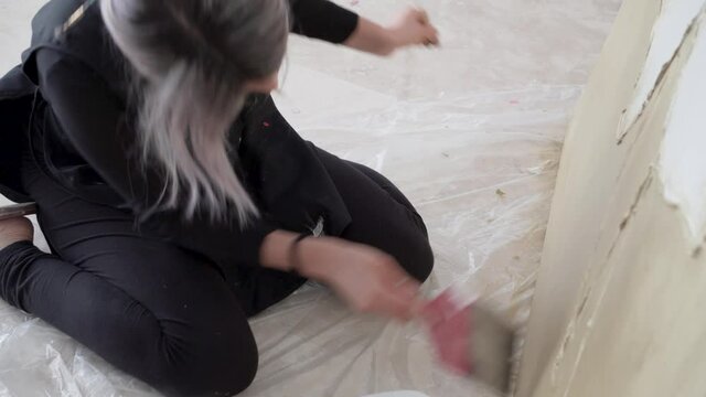 Female Painter With Hair Tied Up Sits On The Floor While Working On Huge Art Canvas. - Low Angle Shot 