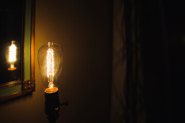 Incandescent bulb. Vintage hanging Edison light bulb in a dark, spooky room with curtains