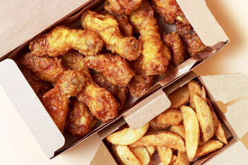 Two boxes with chicken legs and fried potatoes on table, top view.
