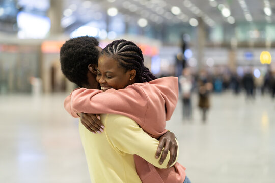 Family reunion in airport. Happy black male hugging excited woman after plane arrival in terminal. Loving coule met after covid-19 epidemic lockdown. Romantic male and female embrace after trip abroad