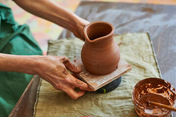 Fototapeta na wymiar A woman master of pottery in a green apron puts a jug of red clay to dry.