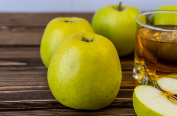 Green apples and glass with apple juice on wooden background
