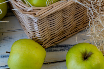 Green apples and basket with apples on wooden background