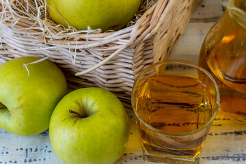 Green apples and jug with glass with apple juice on wooden background