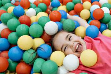 a child in the children's playroom. The girl is having fun among the colorful balls. Dry Pool Party