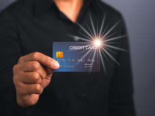 Portrait of a businessman wearing a black shirt holding a mockup blue credit card with star light effect while standing in a studio with copy space for text. Money and business concept