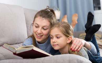 Happy mother with her daughter reading a book on the couch at home. High quality photo
