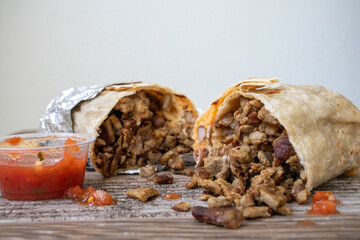 A close-up of a carne asada beef burrito wrapped in foil. It is cut in half and has meat spilling...