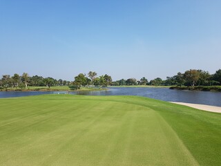 A golf course with a white flag on its hole and a pond and clear sky.