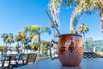 Fresh Moscow mule cocktail with ice, lime and mint leaves in copper mug on swimming pool. Refreshing drink on luxury vacations. Concept summer holiday and travel.
