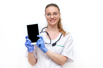 Female doctor in white coat with stethoscope holds it in hands electronic tablet, isolated on white background. Young beautiful woman hospital medical worker looking at camera and smiling. Mock up.