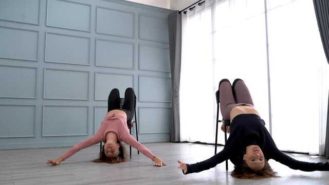 women perform chair dance in studio. young females practice movement of body with leg and arm to balance posture with black chair. dancing in smooth action at studio space with natural daylight.