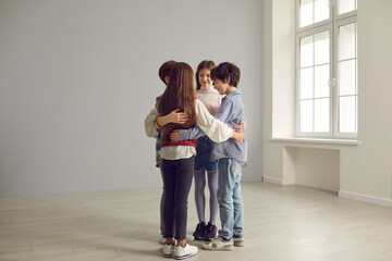 Small group of happy school children standing close in circle. Team of four junior kids huddling in big spacious empty room. Peer interaction, help, cooperation, union, connection, friendship concept