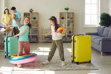 Little twin sisters dance and have fun among the suitcases in anticipation of summer vacation. Family collects things and prepares for a vacation at sea. Concept of active family and travel.