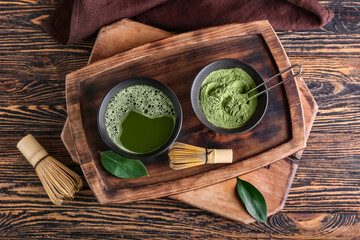 Tray with bowl of matcha tea, powder and chasens on wooden background