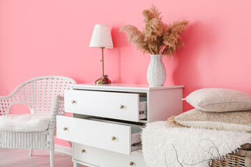 Modern chest of drawers and chair near color wall in room