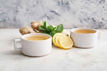 Obraz na płótnie Canvas Cups of tea with ginger, mint and lemon on light background