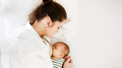 mom and newborn baby, mother breastfeeds the baby lying on a white background on the bed in the bedroom, top view and banner