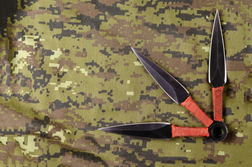Black Throwing knives on camouflage cloth.