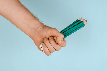 A hand and green wooden pencils on a blue background.