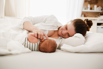 Cute caucasian mom and newborn baby, mom breastfeeds her baby lying on a white background on the...